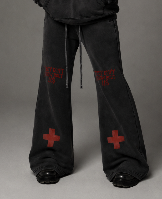 Person wearing a black hoodie and pants with red text and symbols on a gray background